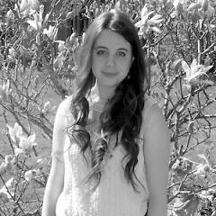 Autorin Yvonne Singer im Portait und lächelt in die Kamera vor einem Blumenbusch