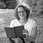 Heike Hamboch Portrait zeigt die Autorin vor einem ländlichen Hintergrund mit einem Buch in der Hand. Sie lächelt in die Kamera.