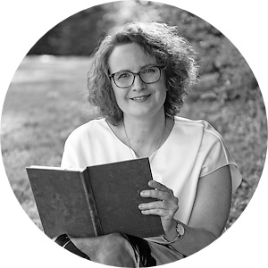Heike Hamboch Portrait zeigt die Autorin vor einem ländlichen Hintergrund mit einem Buch in der Hand. Sie lächelt in die Kamera.