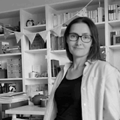 Autorin Karin Bell steht vor ihrem Bücherregal und lächelt in die Kamera