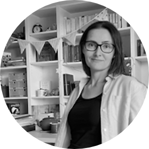 Autorin Karin Bell steht vor ihrem Bücherregal und lächelt in die Kamera